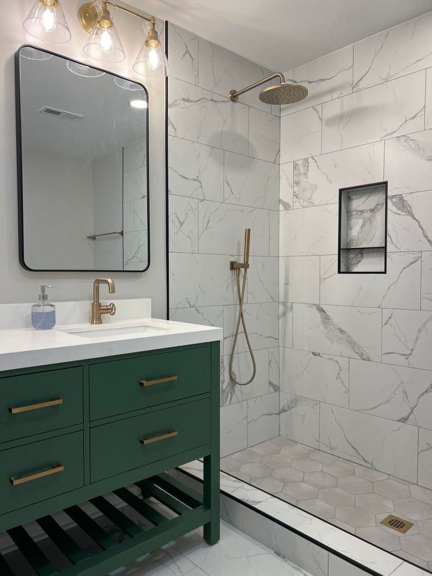 Modern bathroom with green vanity, gold fixtures, large mirror, and marble-tiled shower.