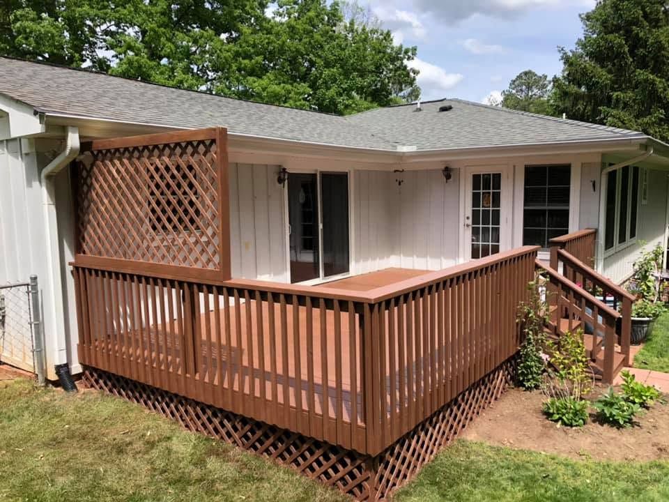 Back deck with brown railing and lattice, connected to a white house with sliding glass doors.