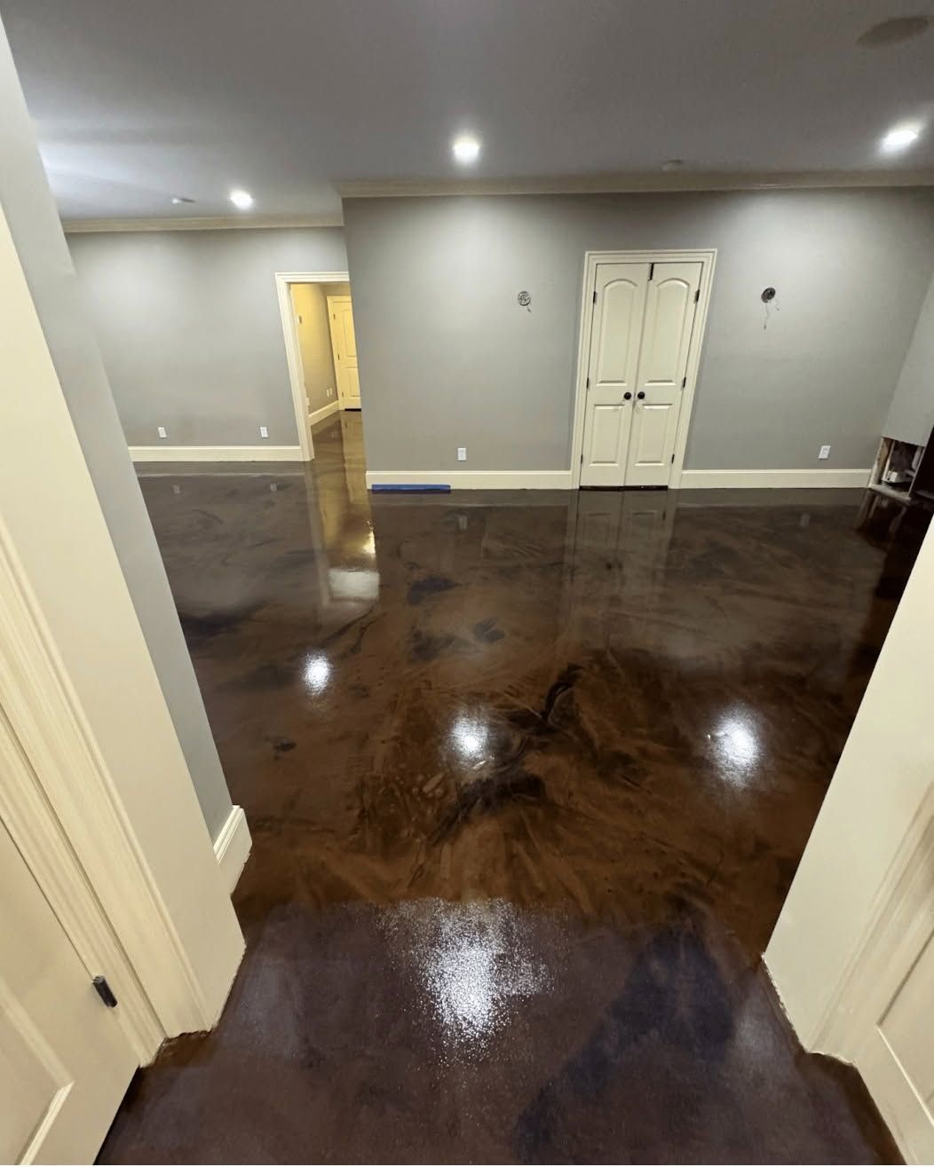 Empty hardwood-floored room with white walls, recessed lights, and a closed white double door.
