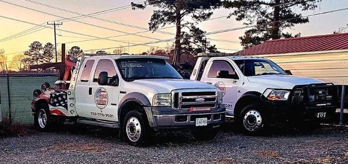 Two tow trucks are parked next to each other in a gravel lot.