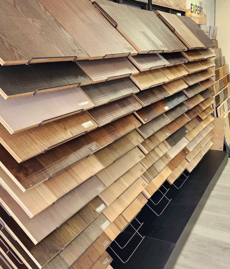 Stacked wood flooring samples displayed in a showroom aisle, showing various brown finishes.