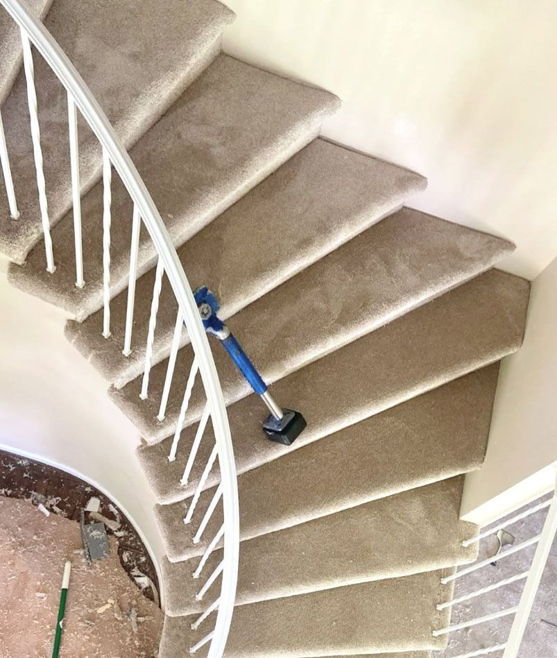 Blue stair-climbing vacuum on beige carpeted staircase with white railing