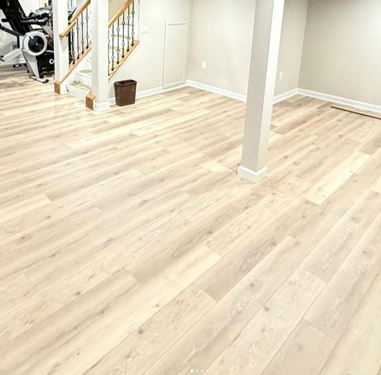 Bright empty room with light wood floors, white walls, staircase, and a small basket near the stairs