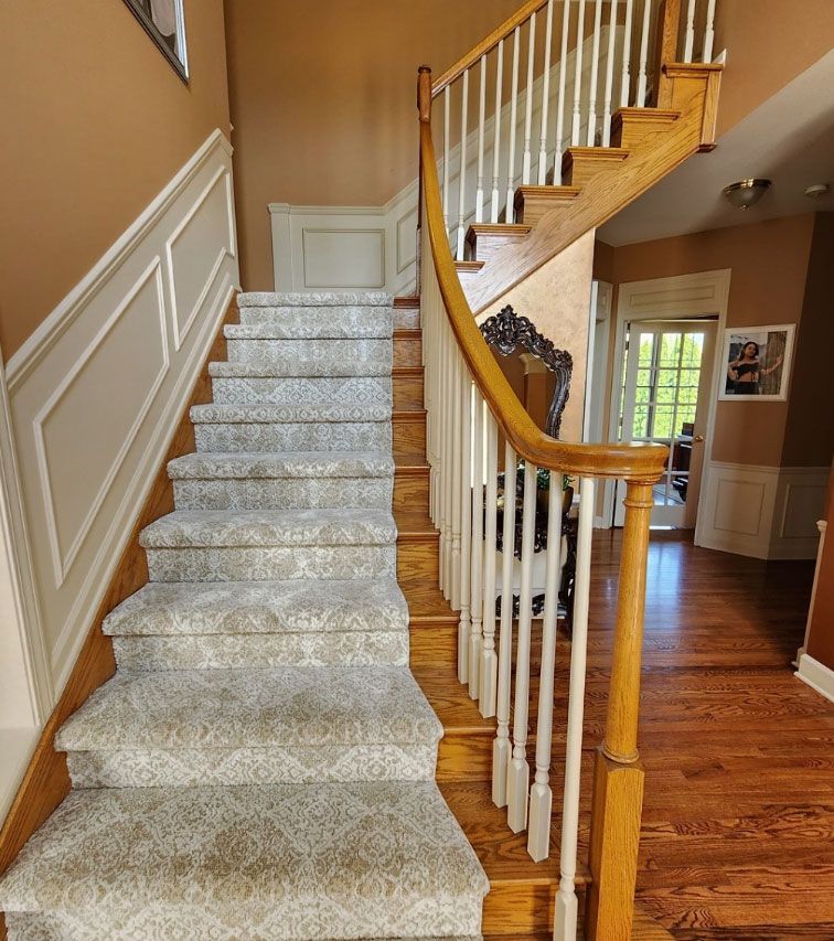 Carpeted staircase with white railing and curved wooden banister in a tan hallway