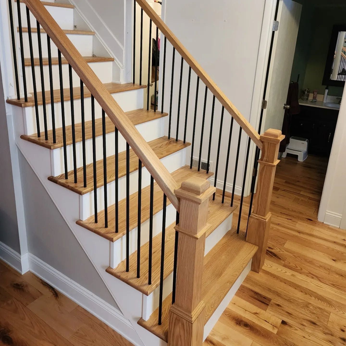 Wooden staircase with black iron balusters and hardwood floors in a bright home interior