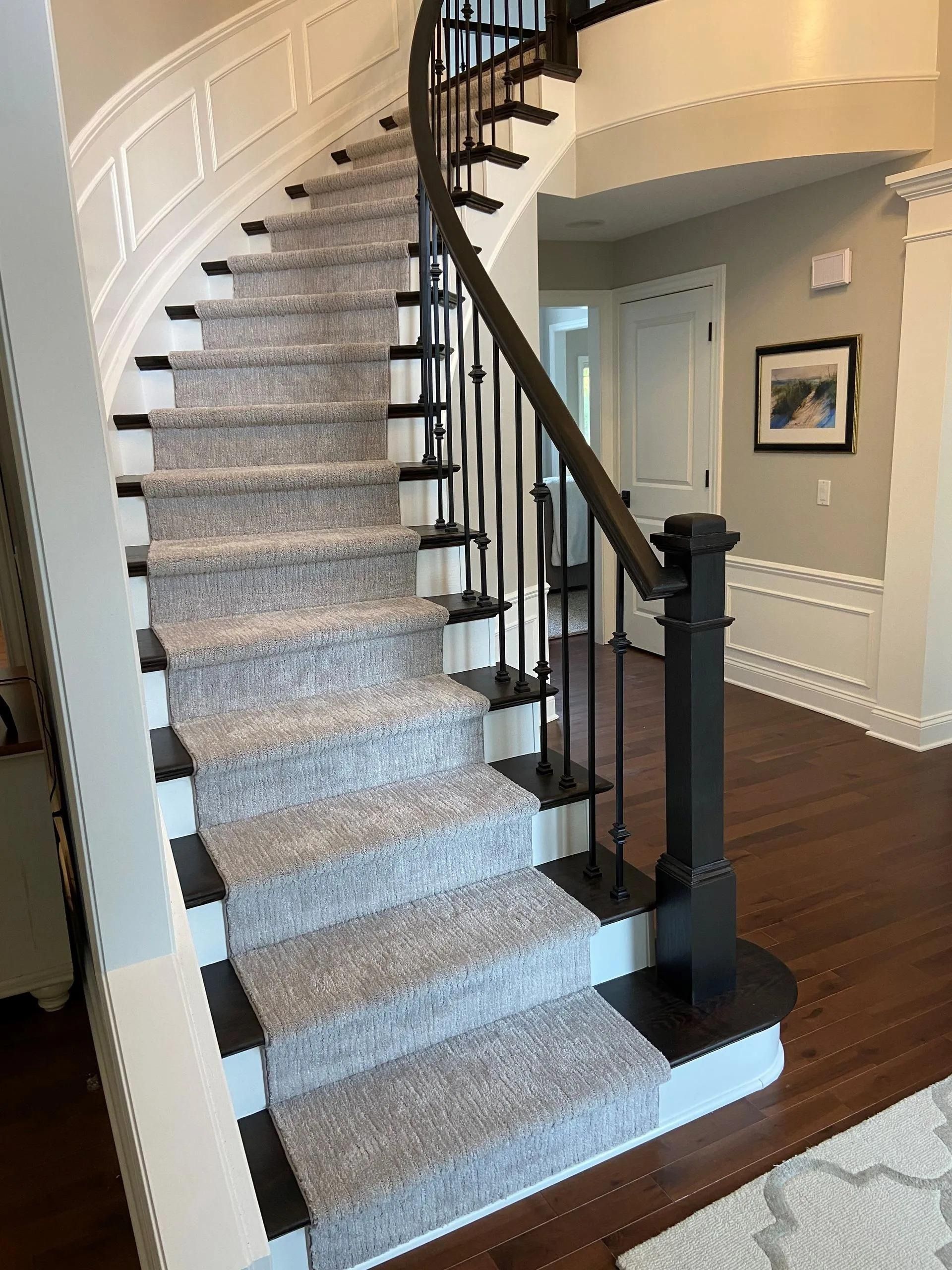 Curved carpeted staircase with dark wood railing in a gray entryway with hardwood floors