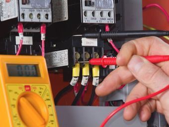 Person using a multimeter to test electrical wires inside a panel. The meter reads 0.00 volts.