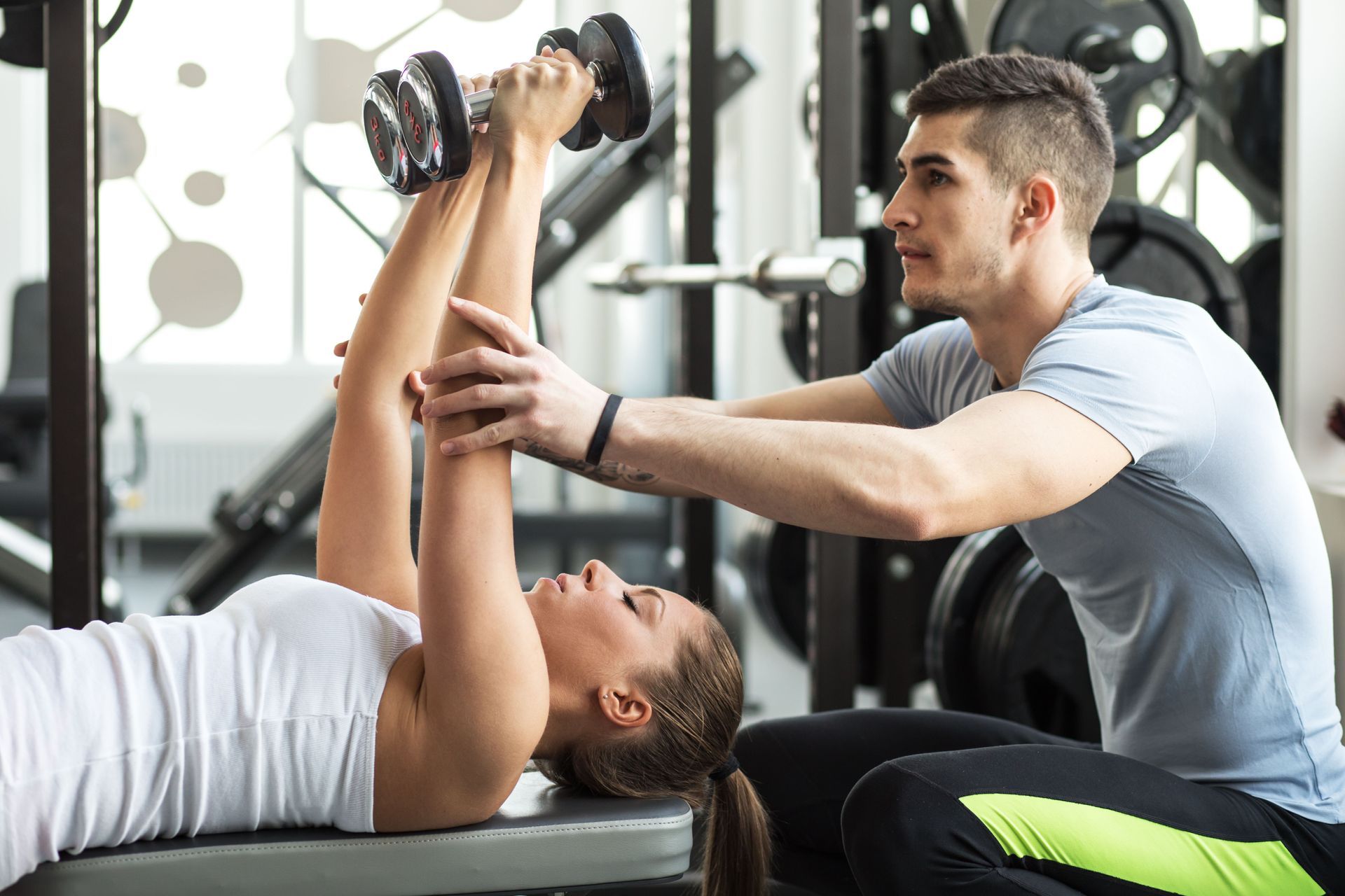 Trainer assisting client with dumbbell exercise in a gym