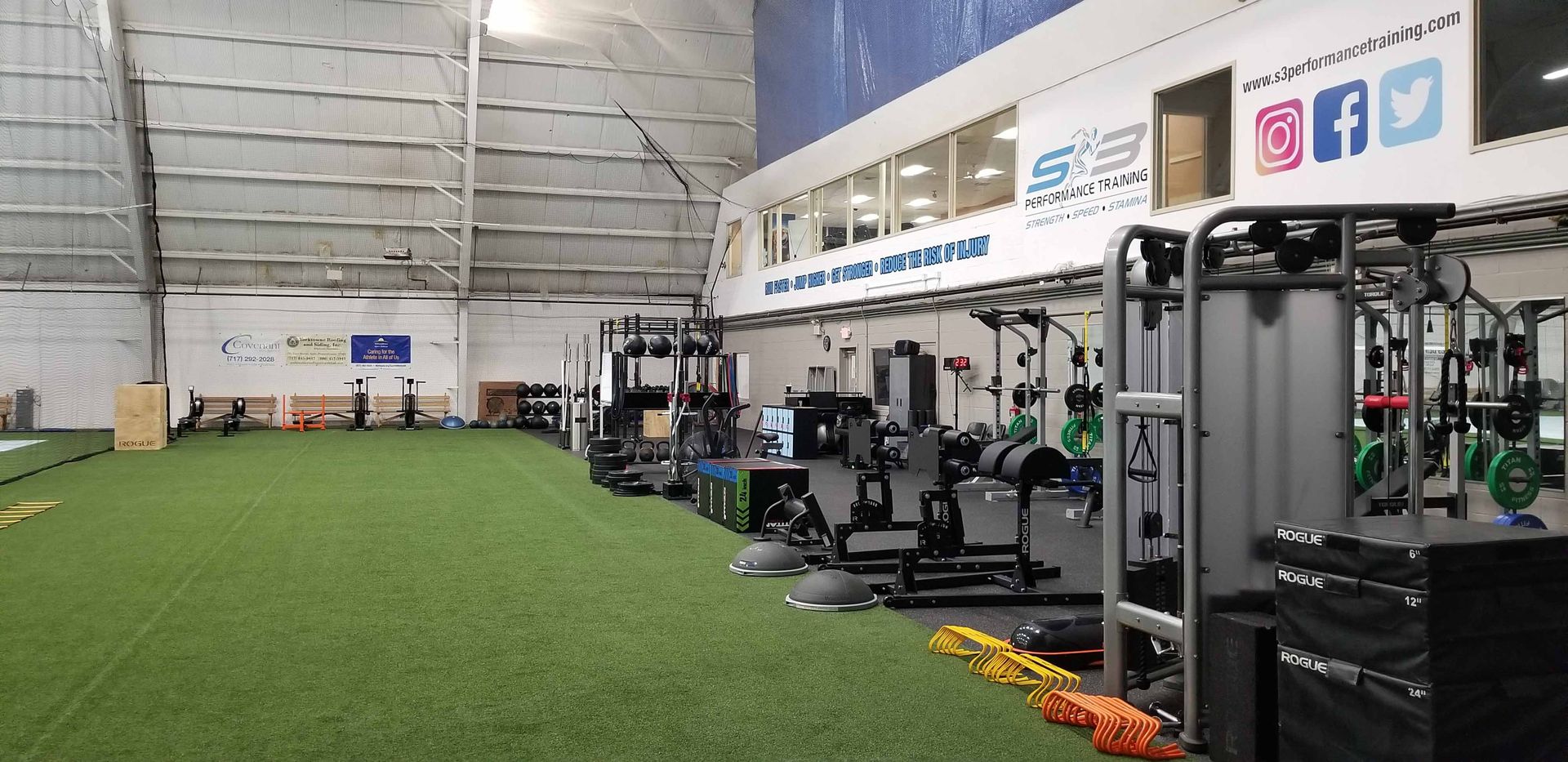 Indoor gym with green turf, weight machines, and exercise equipment along the wall