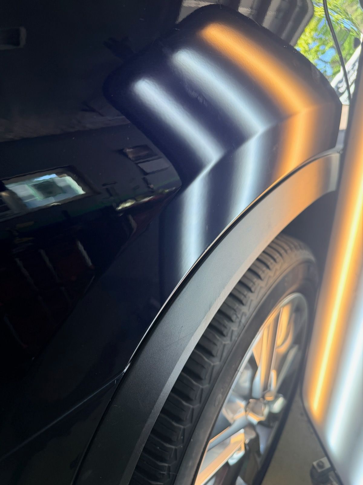 Close-up of a black car’s front fender and wheel with bright orange and white reflections