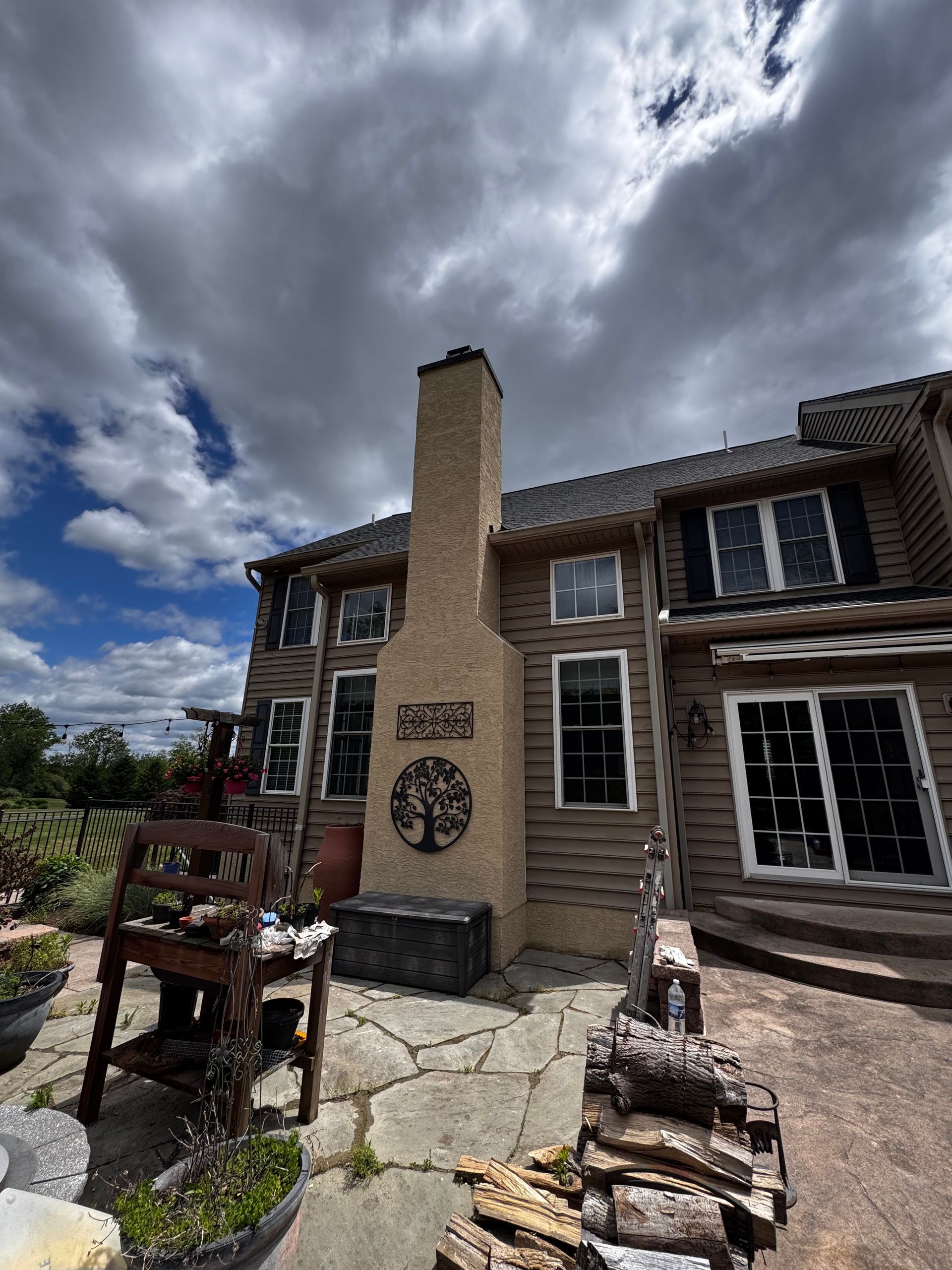 Stone patio and brick house exterior with a tall chimney under a cloudy sky
