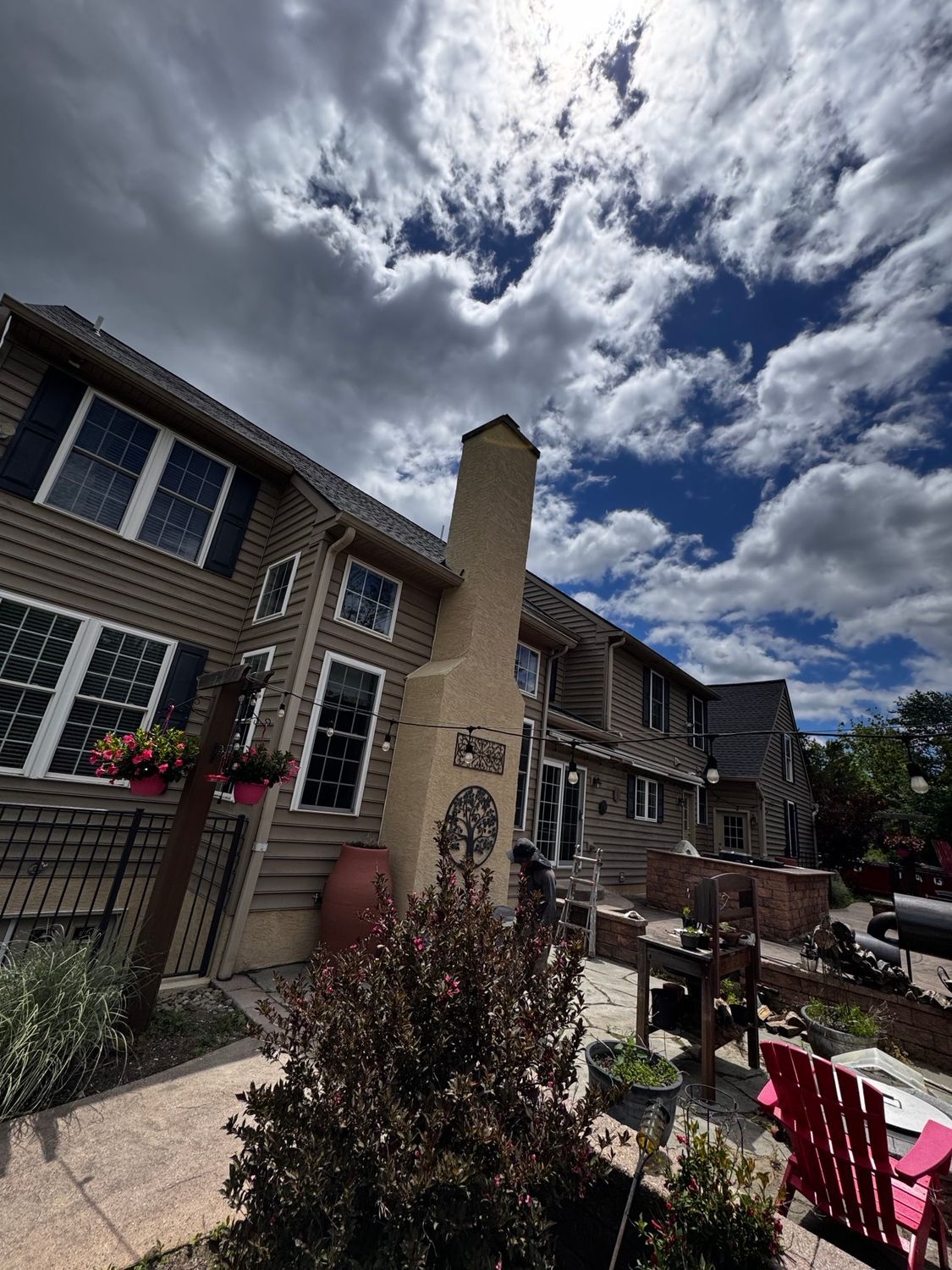 Brick townhouse patio with pergola, flower pots, and red chairs under a cloudy sky