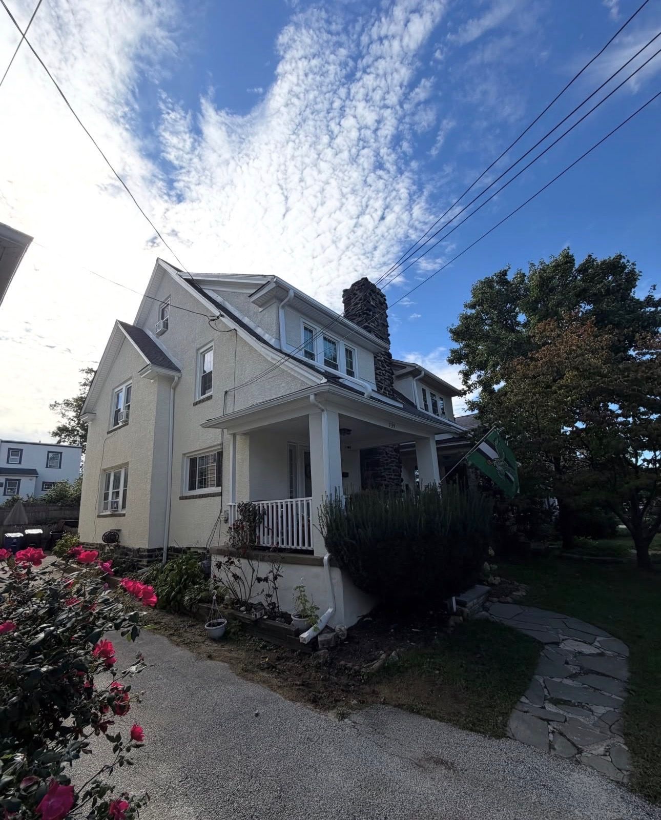 White two-story house with porch, gravel path, and flowers under a bright blue sky