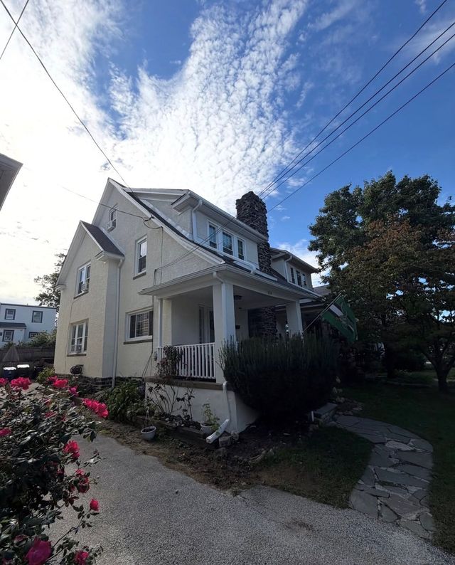 White two-story house with porch, gravel path, and flowers under a bright blue sky