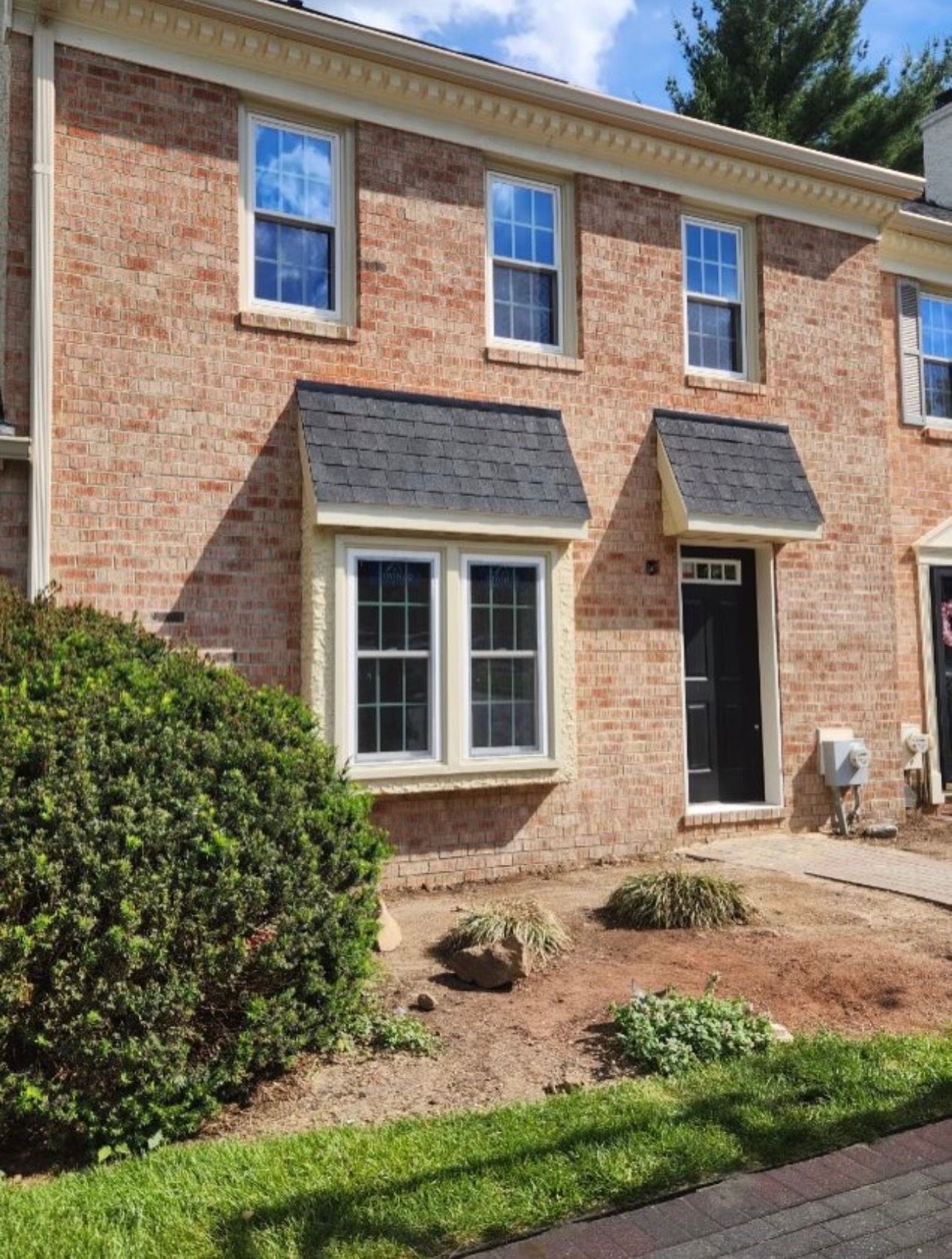Brick townhouse exterior with black front door, white-trimmed windows, and landscaped front yard