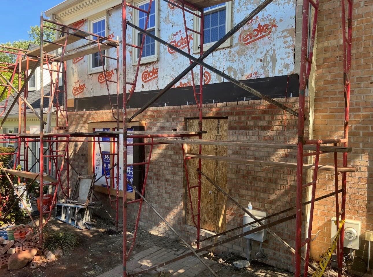 Scaffolding around a two-story house under construction, with workers and building materials visible