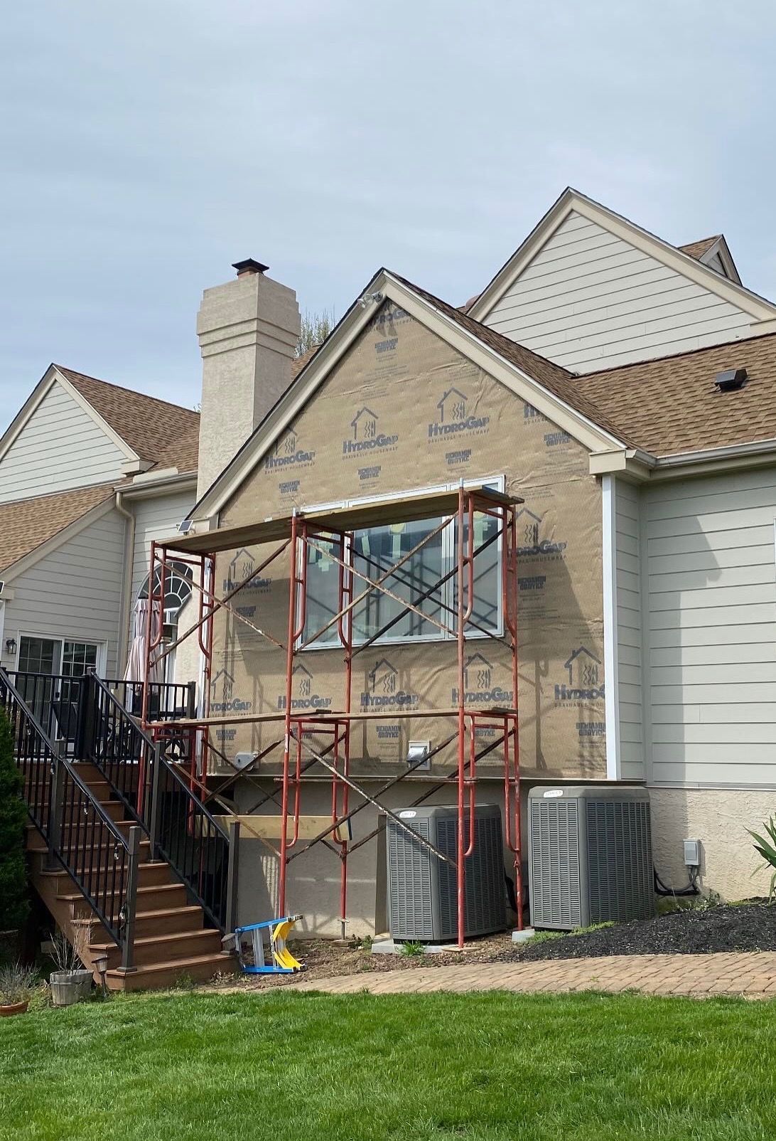 House front under construction with red scaffolding, boarded windows, and a brick chimney.