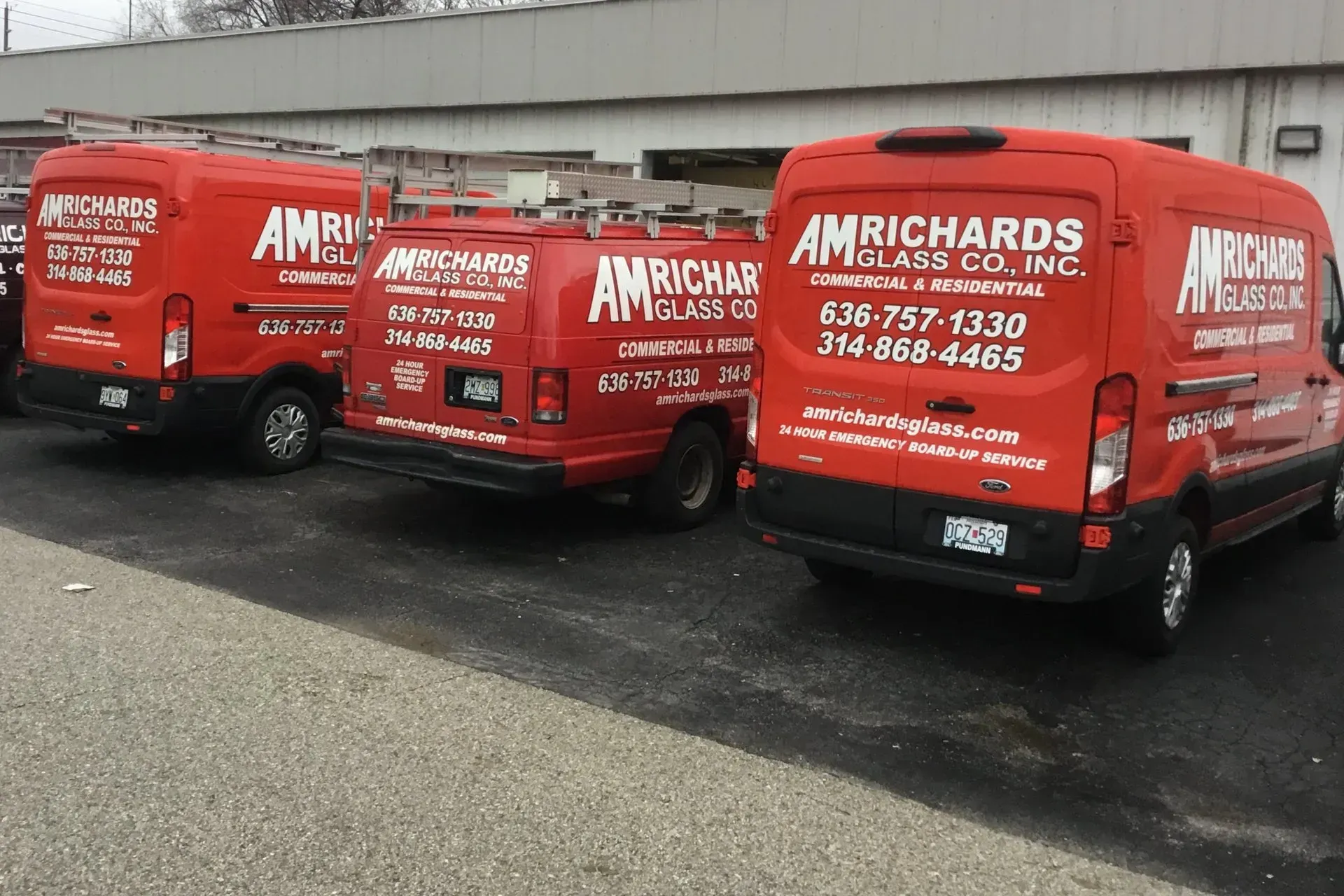 Three red AM Richards Glass Co. vans parked outside a building.