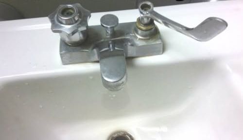 A chrome bathroom sink faucet with two mismatched handles—a star-shaped knob and a long lever—mounted on a white sink.