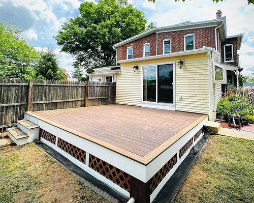 Raised wooden backyard deck beside a beige house with sliding glass doors and a fenced yard