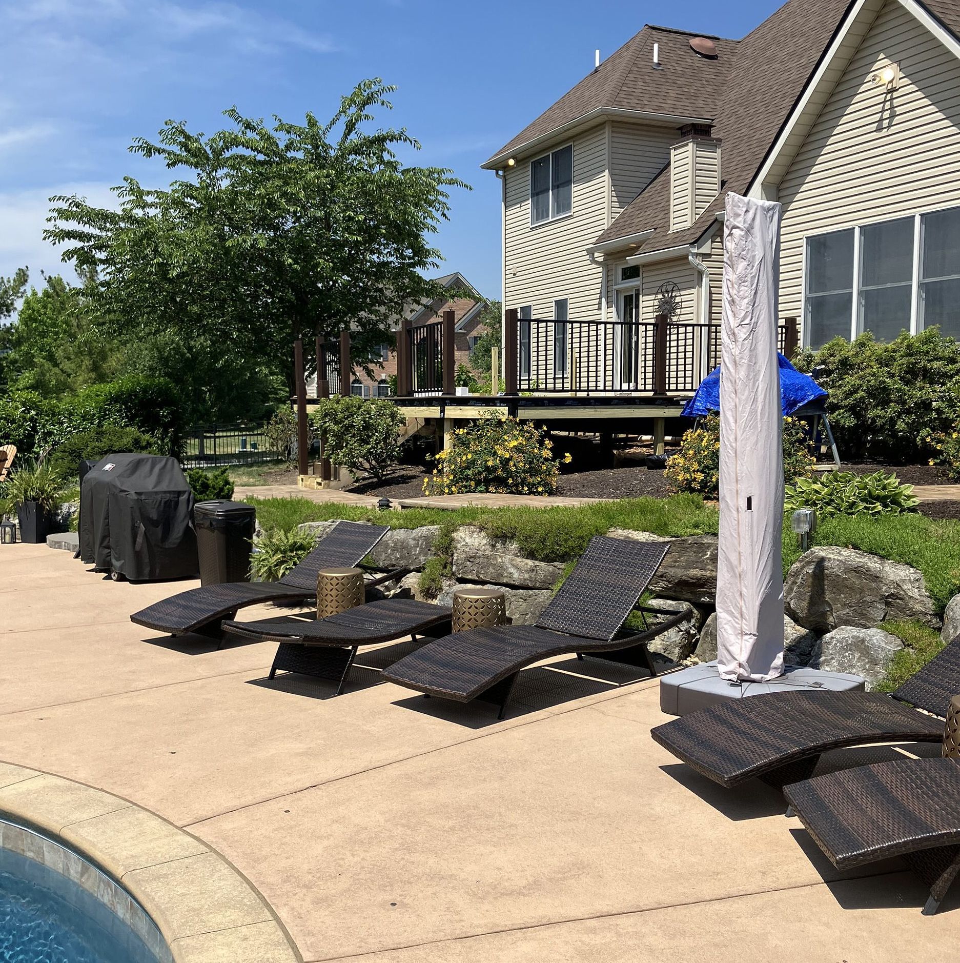 Poolside patio with black lounge chairs, a grill, and a two-story house in the background