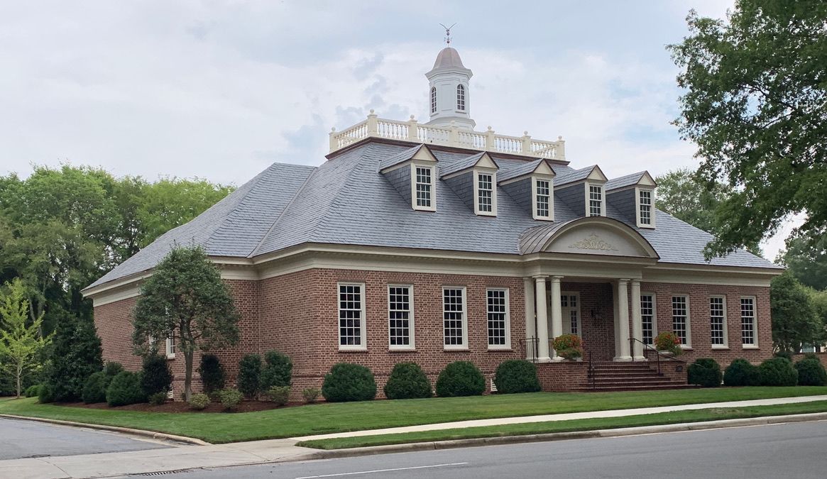 Two aerial views of a brick building with a slate roof. The top shows dormers and chimneys. The bottom view shows the roof's shape.