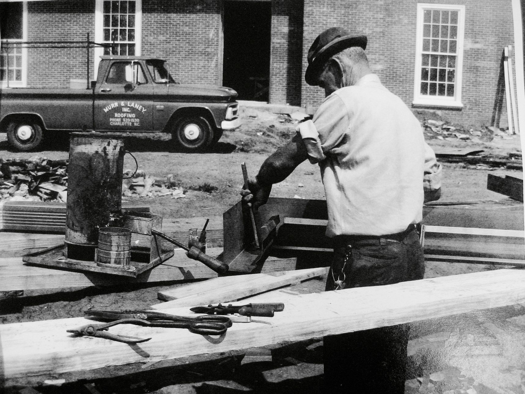 Man using a saw to cut lumber outdoors next to a vintage pickup truck.