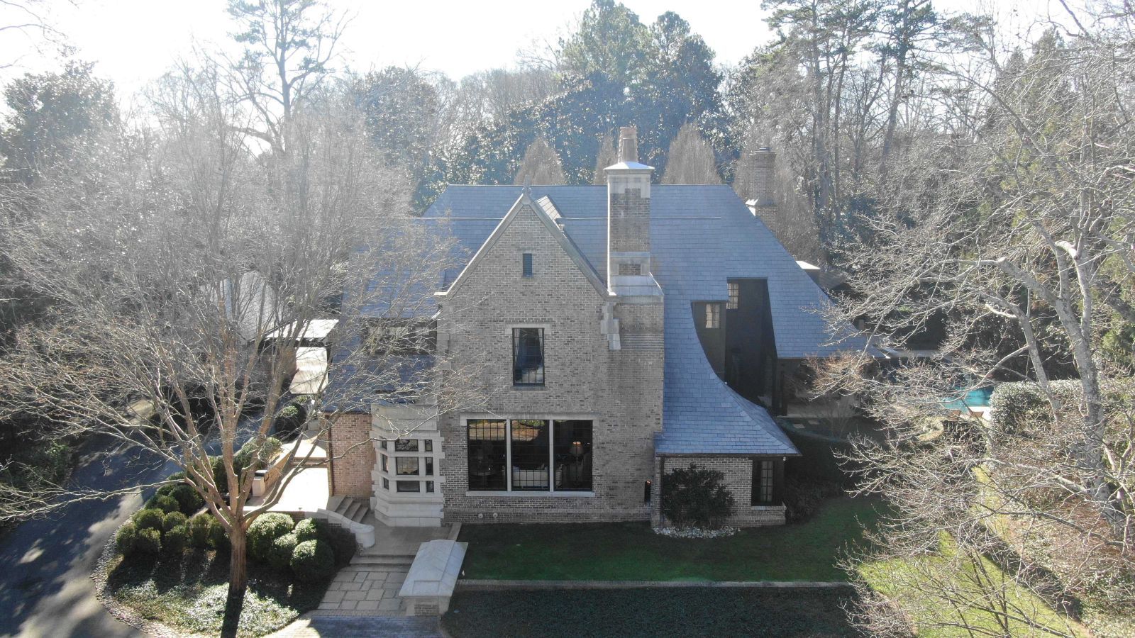 Stone house with a steeply pitched gray roof, a large front window, and chimneys, surrounded by bare trees.