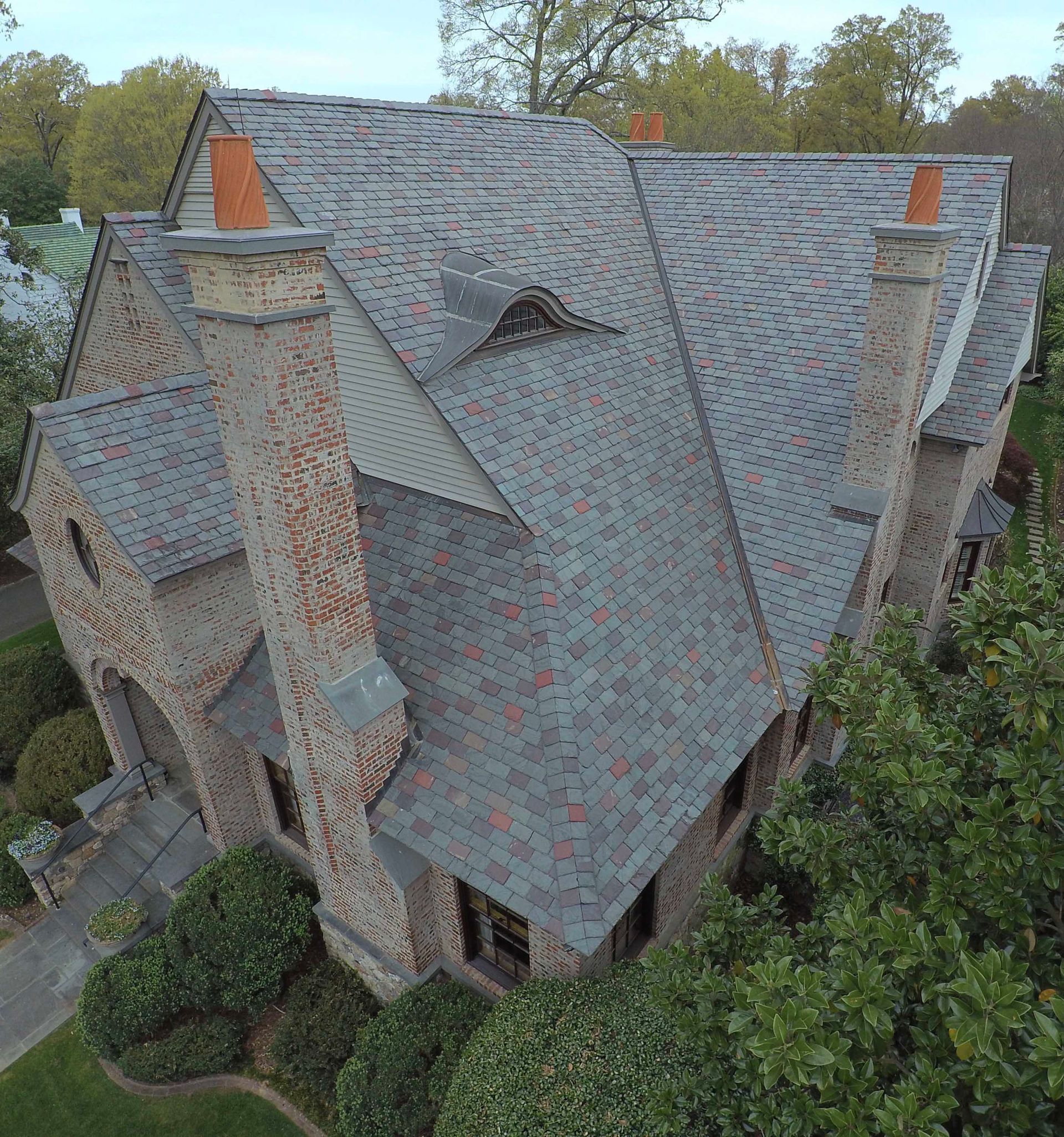 Stone house with a multi-gabled roof, chimneys, and surrounding greenery.