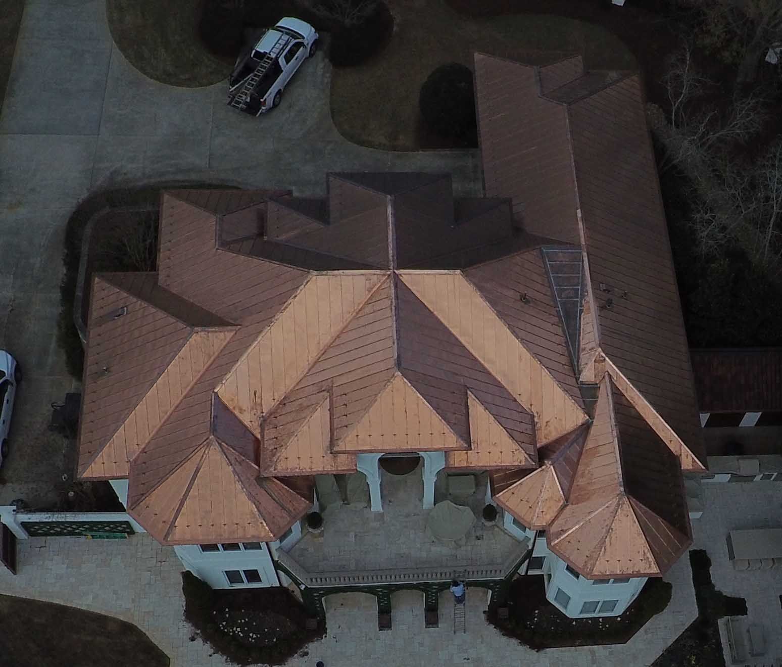 An aerial view of a large house with a copper roof. A white truck is parked in the driveway.