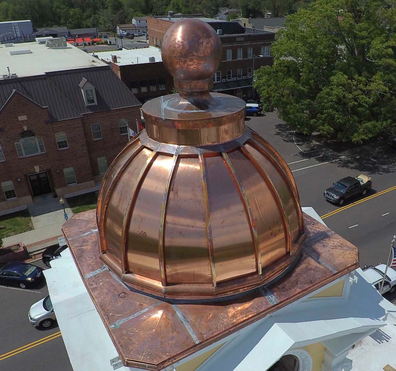 Copper dome on a building rooftop in a town square. Shiny metal reflects the surrounding buildings and sky.