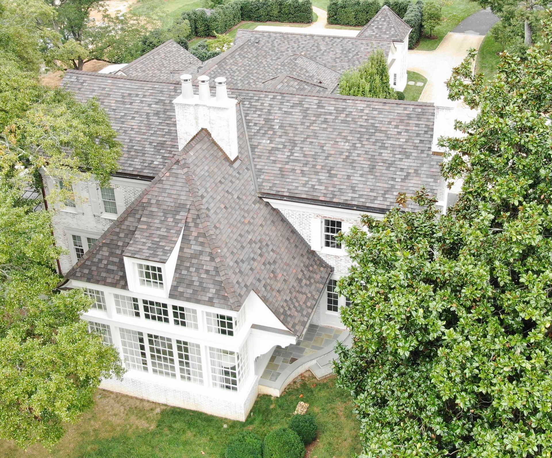 Aerial view of a large, white-brick house with a gray roof and surrounded by trees.