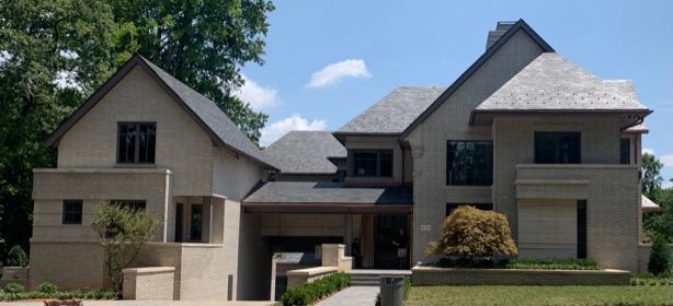 Large beige house with dark roof and trim under a blue sky.