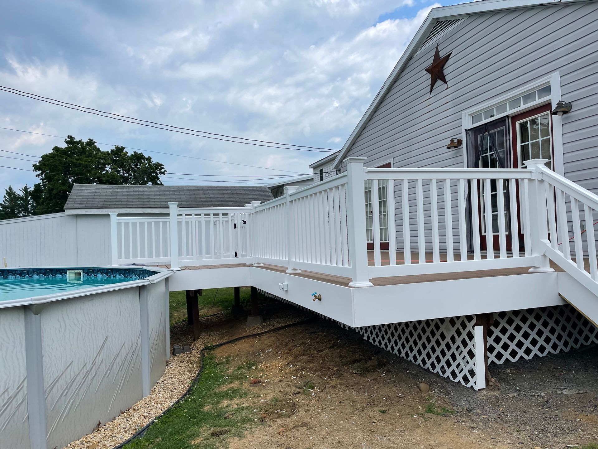 A white deck with railings connects to an above-ground pool next to a gray house with a metal star decoration.