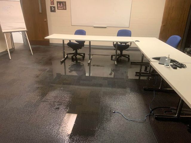 Flooded conference room with tables, chairs, whiteboard, and a flip chart. Dark, wet floor.