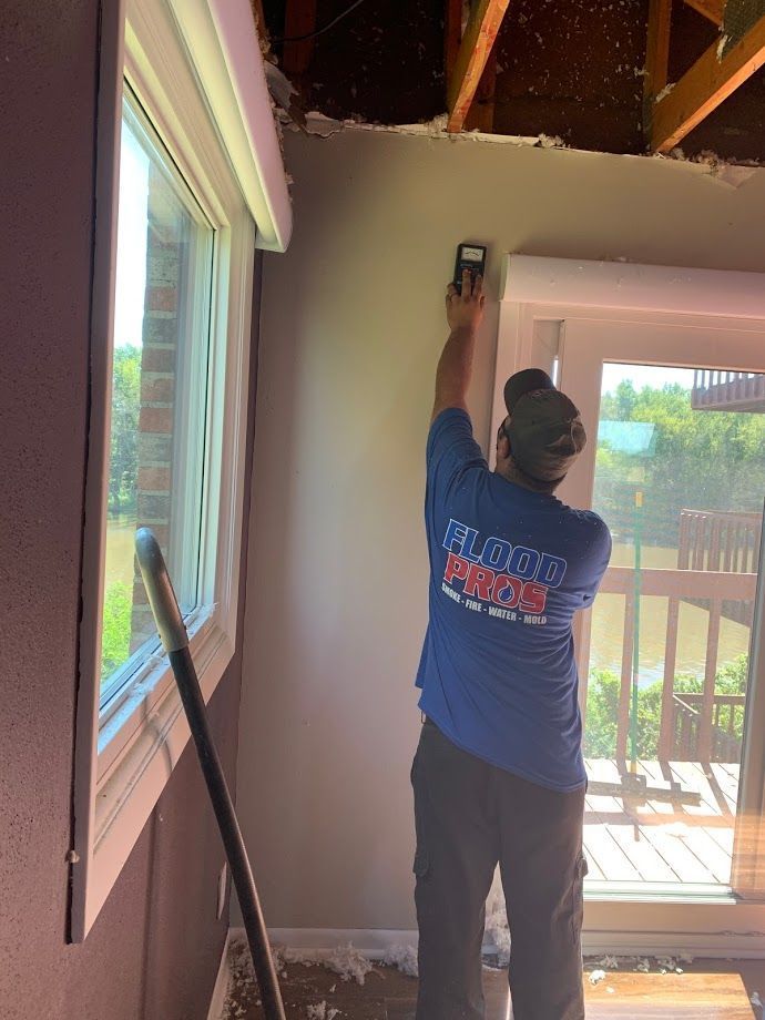 Person in blue shirt measures a wall with a device inside a room. Window and door visible.