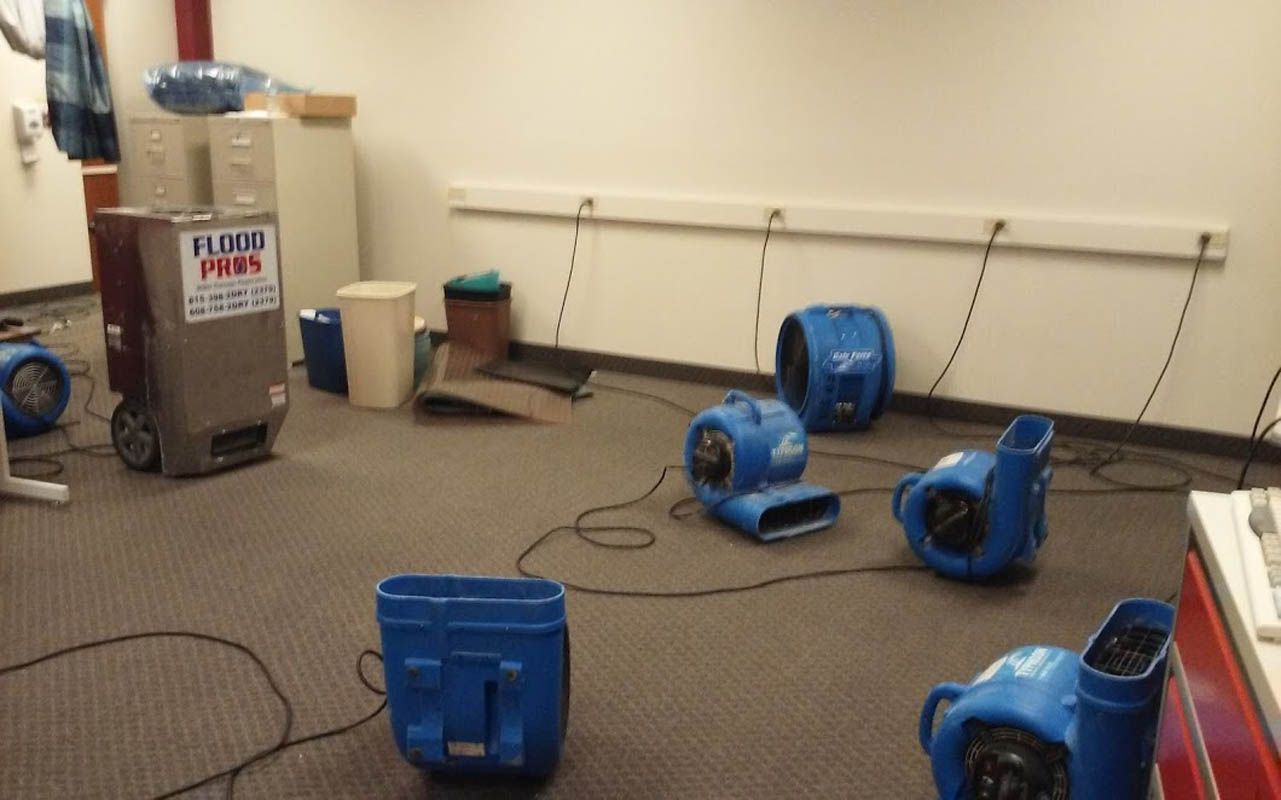 Room with several blue fans and a large dehumidifier; likely water damage cleanup.