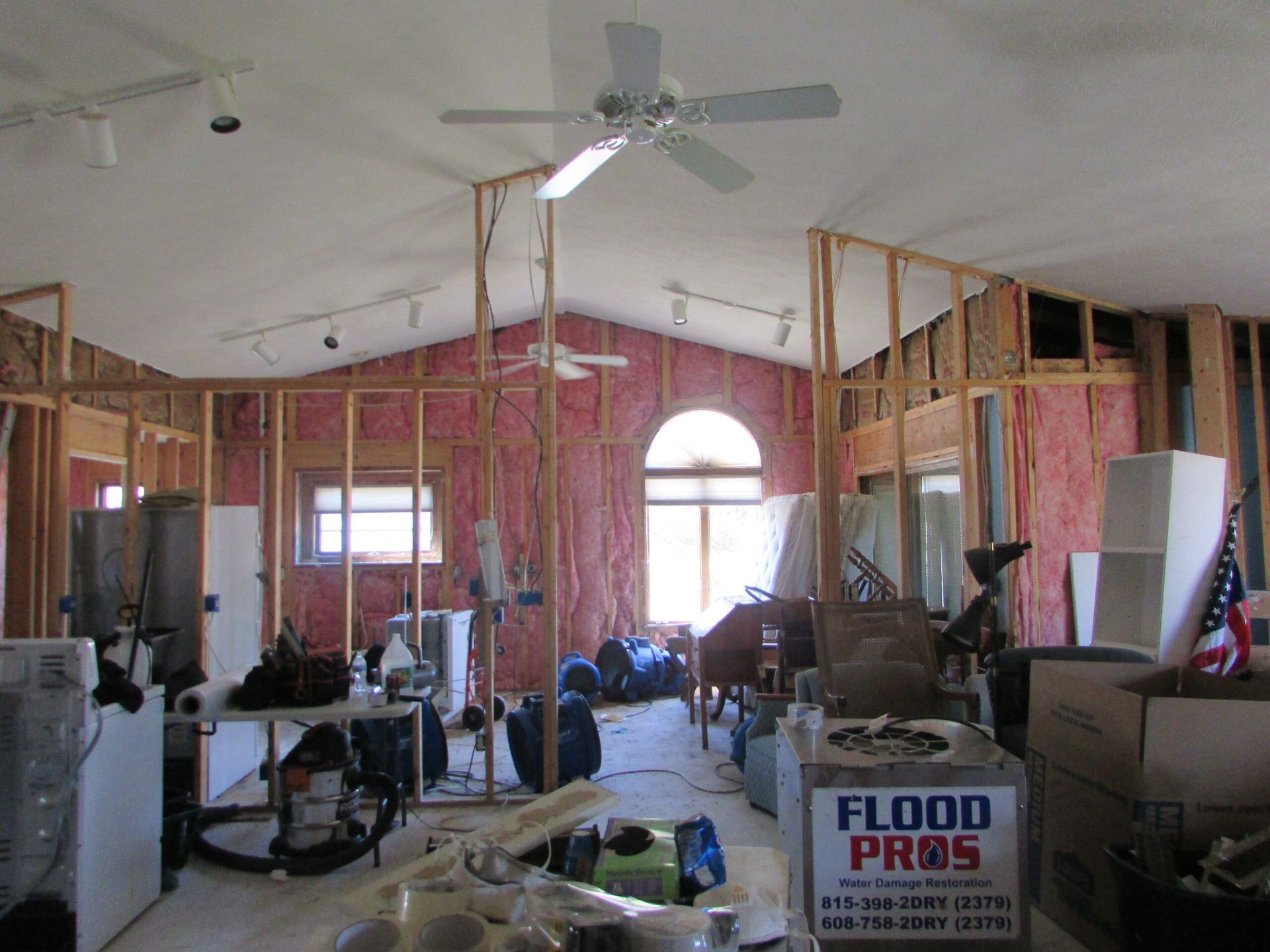 Interior framing of a house under construction with exposed pink insulation and a ceiling fan.
