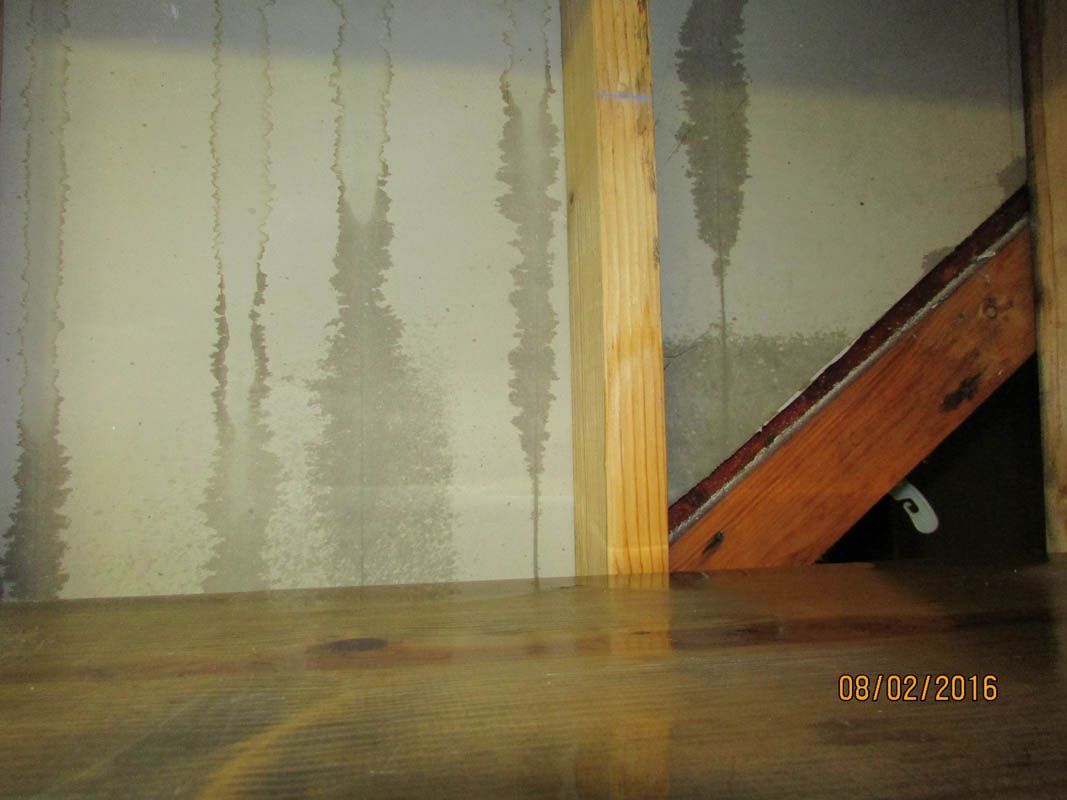 Water damage on wall and floor, likely from leaks. Wooden beams are visible.