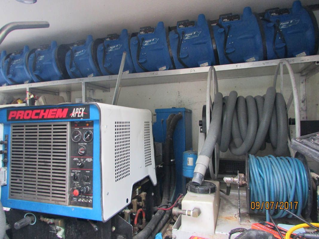 Inside a carpet cleaning truck, Prochem machine, blue hoses, and air movers on shelves.