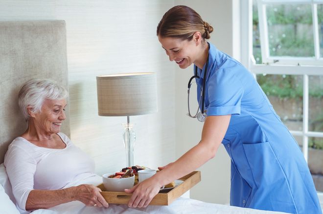 A nurse is serving food to an elderly woman in a hospital bed.