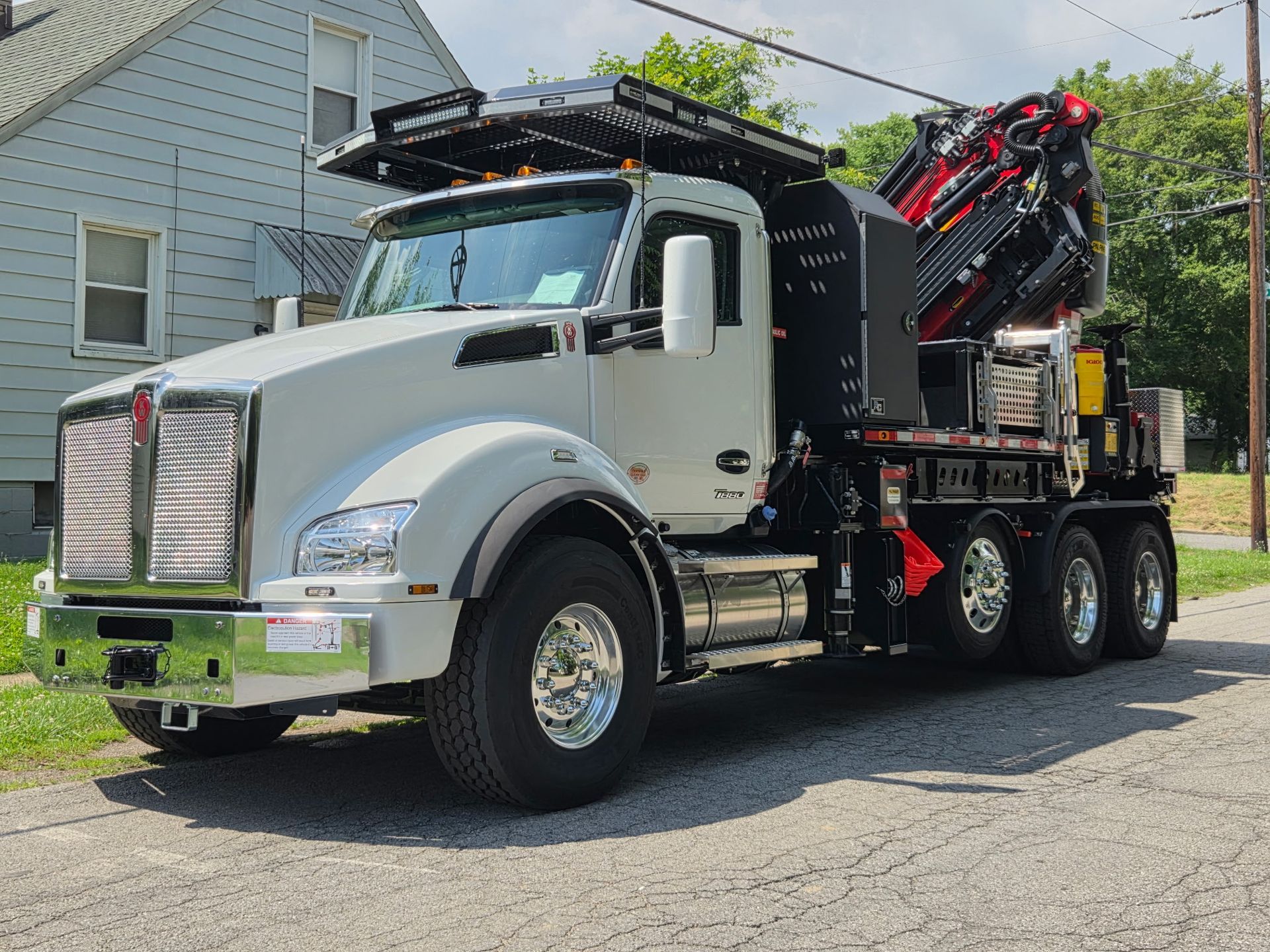 White dump truck with a crane boom parked beside a house on a sunny day