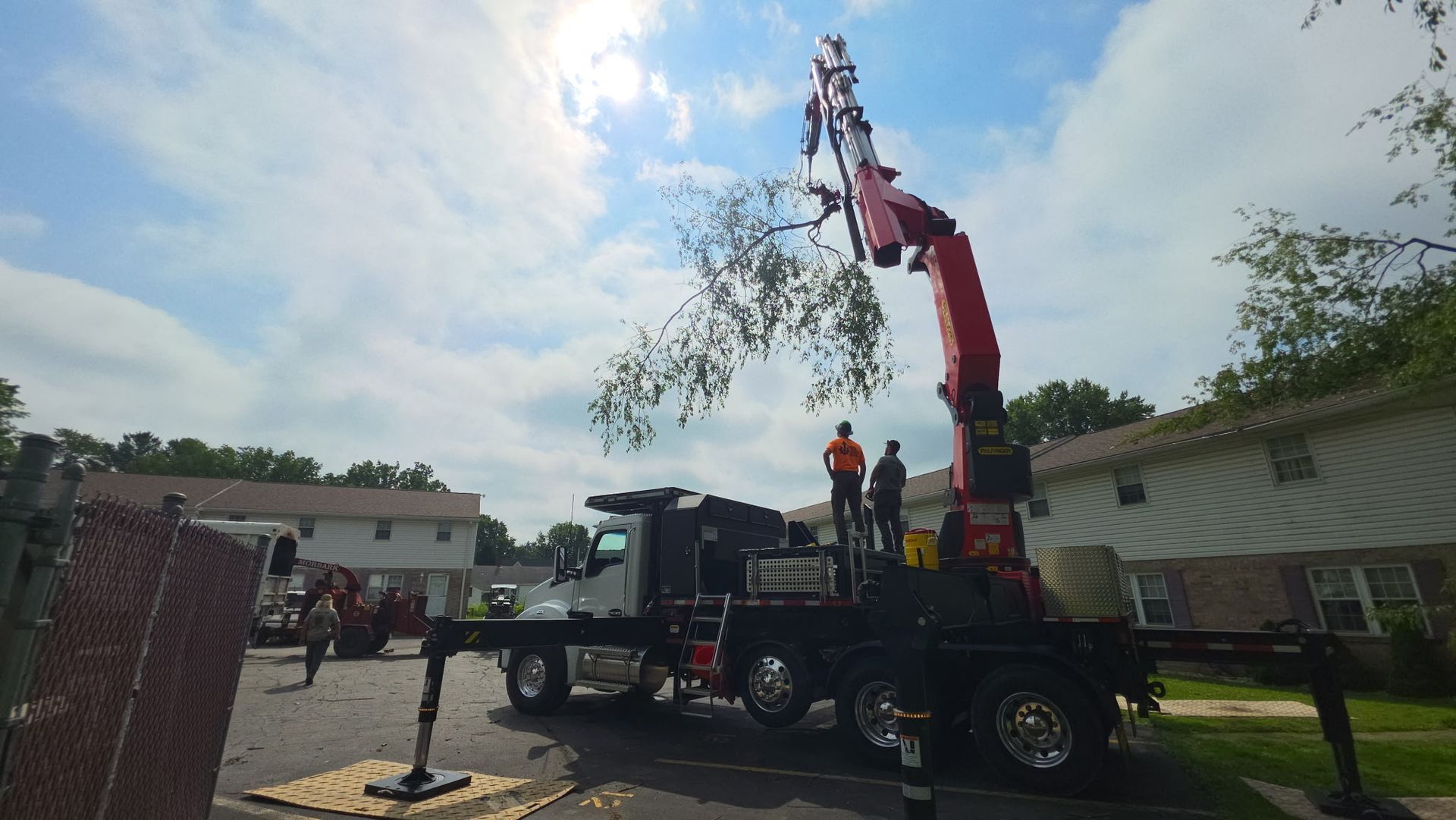Utility truck with extended crane lifting a worker over a residential street under a cloudy sky