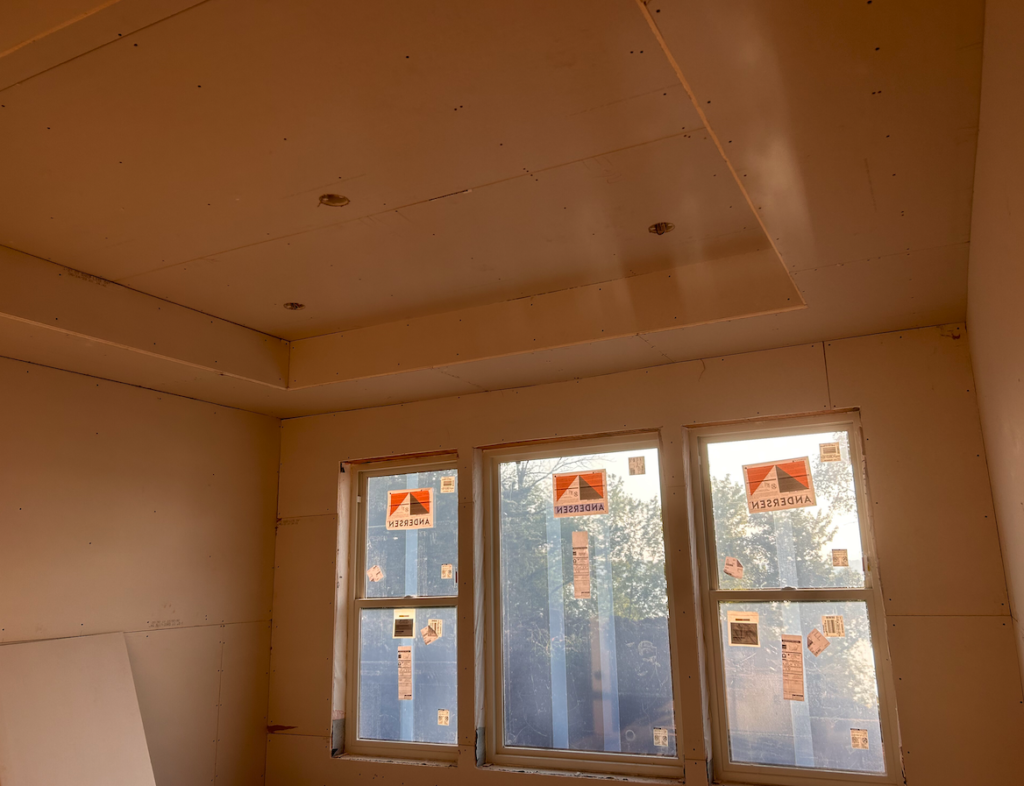 A room with three windows and a ceiling that is being built.