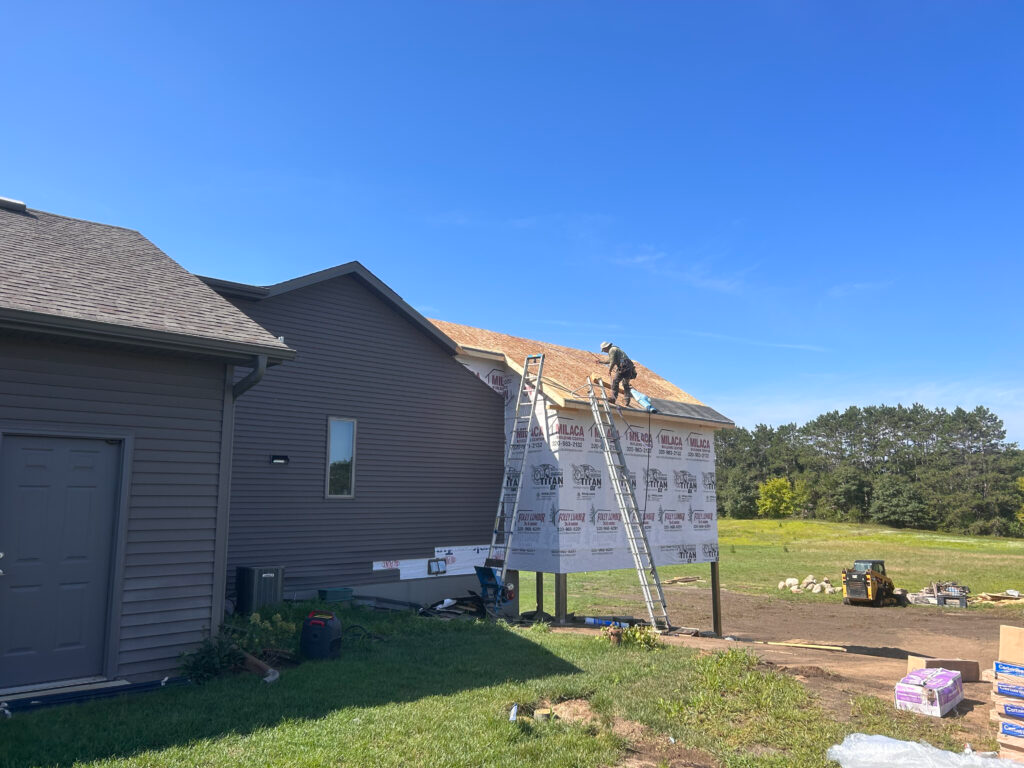 A man is standing on a ladder on the roof of a house.
