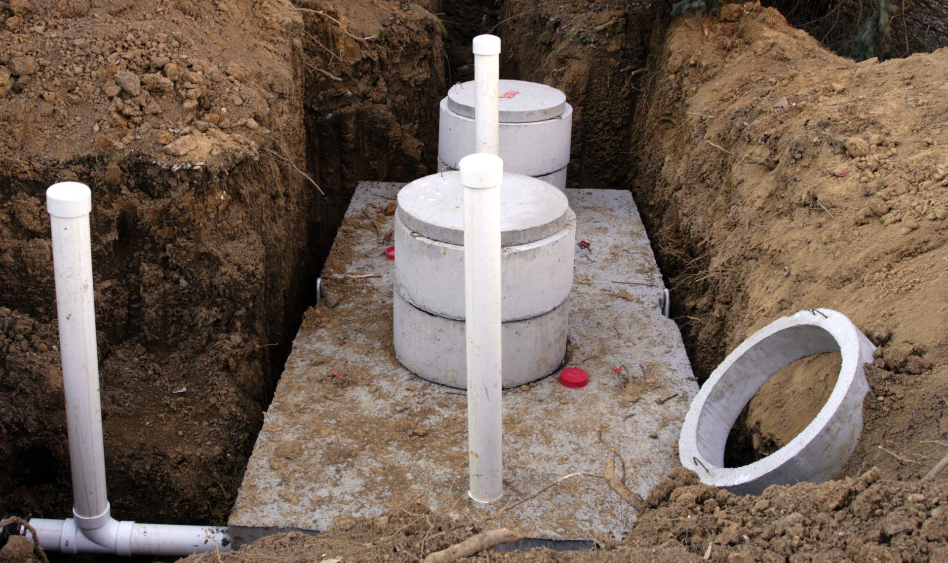 Septic tank installation with white PVC pipes and concrete chambers in a trench
