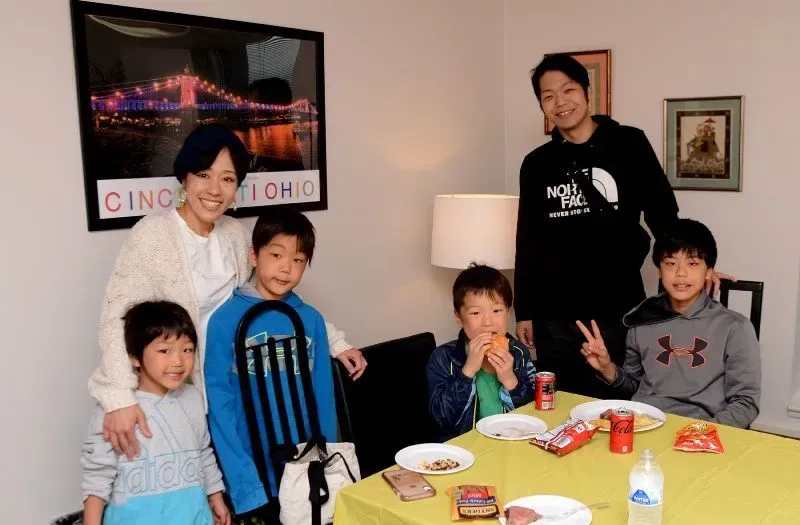 Family poses around a table with snacks and drinks; Cincinnati artwork on the wall.
