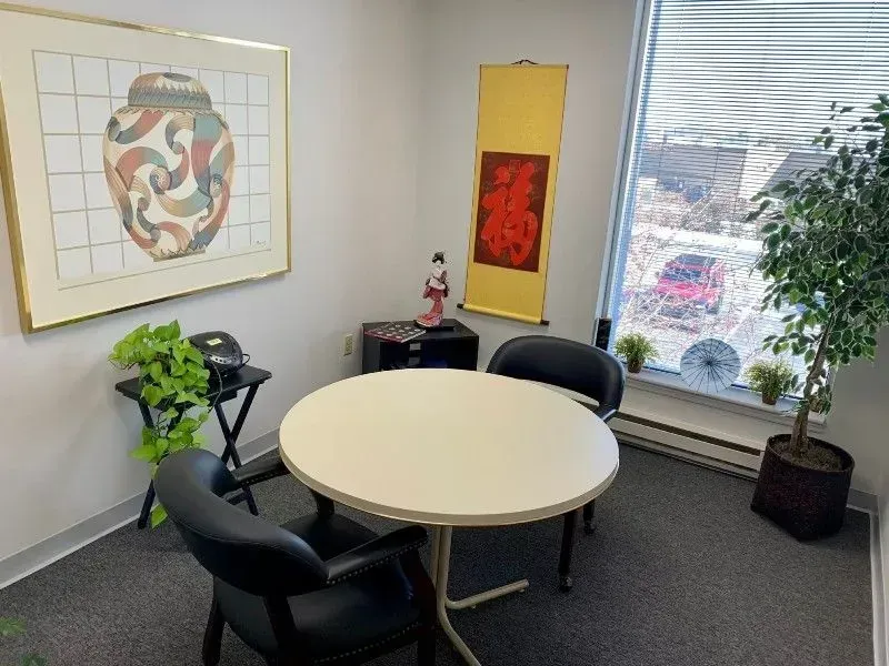 Small office with round table, chairs, artwork, and a window with a partial view of outside.