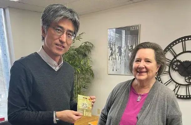 Man holding item smiles next to smiling woman in office setting with clock and art on wall.