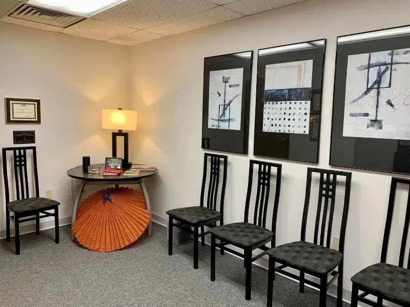 Waiting room with chairs, artwork, round table, lamp, and orange parasol.